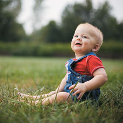Baby in red shirt and overalls sitting on grass
