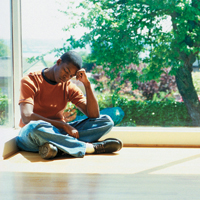 young man sitting by window with head down on fist, looking sad