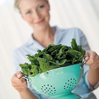 Woman holding blue colander full of leafy greens