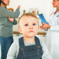 Toddler in overalls, mother speaking to doctor behind him