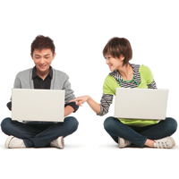 Two people sitting on ground cross legged holding laptops and talking