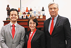 Samuel Cavas and Barbara Gordon standing with Senator Sheldon Whitehouse, wearing red tie