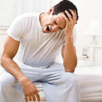 Man dressed in white, sitting on bed, yawning