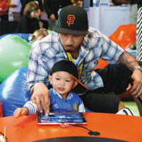 Father and son wearing matching SF Giants hats, playing on iPad