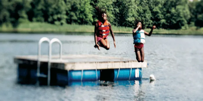 Kids jumping into a lake off of a floating dock