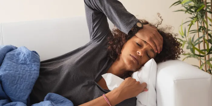 A woman with a cold laying down and holding her head