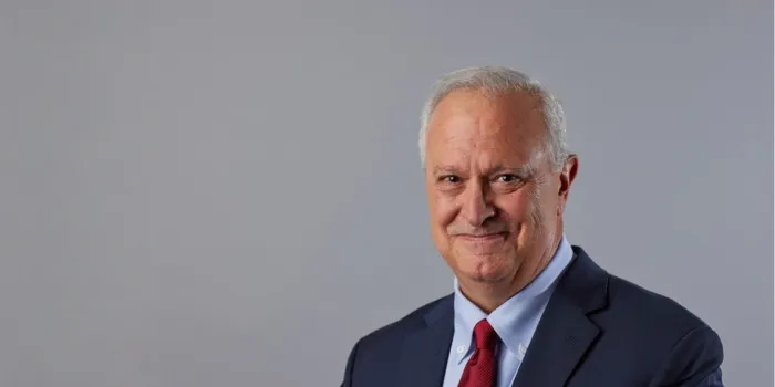 Headshot of Phil Gattone wearing a dark suit, light blue shirt, and red tie, against a gray background.