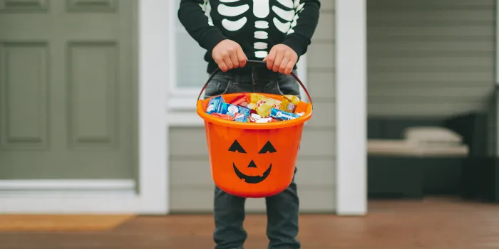 A child wearing a skeleton sweater and holding a bucket of candy on Halloween