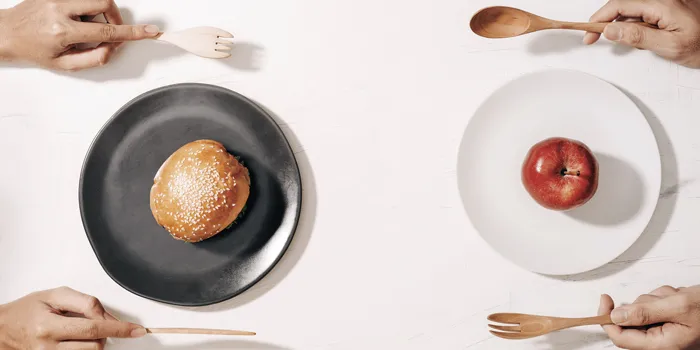 Two plates across from each other on a table, one with a burger bun and one with an apple.