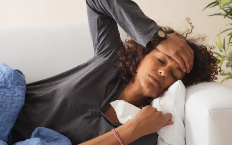 A woman with a cold laying down and holding her head