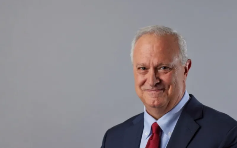 Headshot of Phil Gattone wearing a dark suit, light blue shirt, and red tie, against a gray background.