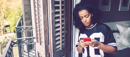 Teen girl looking at smartphone in a room with window open.