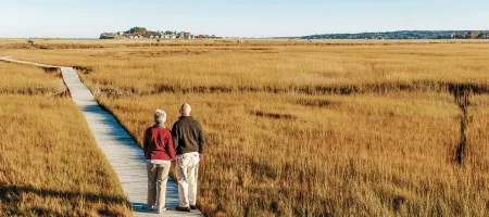 Older couple walking on boardwalk through grassland