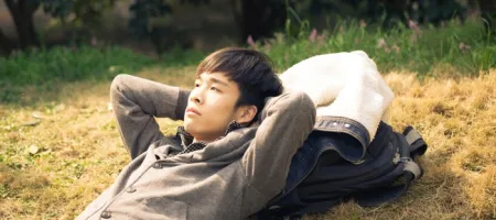Man lies back in the grass with his hands behind his head, resting with his jacket and backpack beside him.