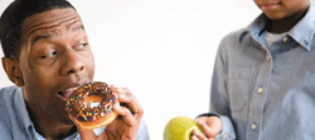 Boy handing an apple to man about to eat a donut