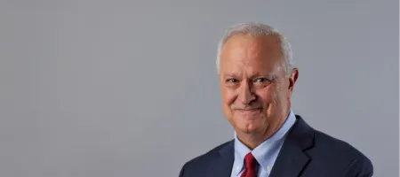 Headshot of Phil Gattone wearing a dark suit, light blue shirt, and red tie, against a gray background.