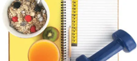 Bowl of granola with fruit and juice on top of open lined notebook with yellow measuring tape, pencil and blue hand weight