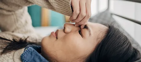 A woman lying down on her bed with a headache while holding the bridge of her nose