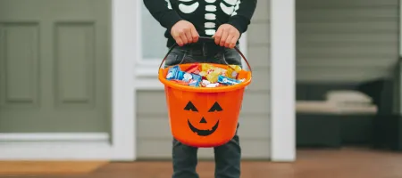 A child wearing a skeleton sweater and holding a bucket of candy on Halloween