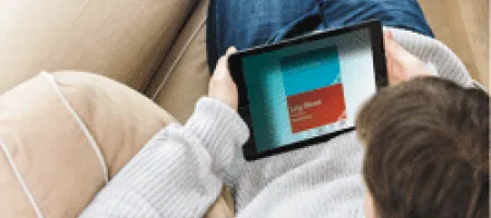 Individual sitting on couch reading tablet