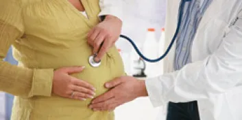 Doctor using stethoscope to examine pregnant woman