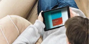 Individual sitting on couch reading tablet